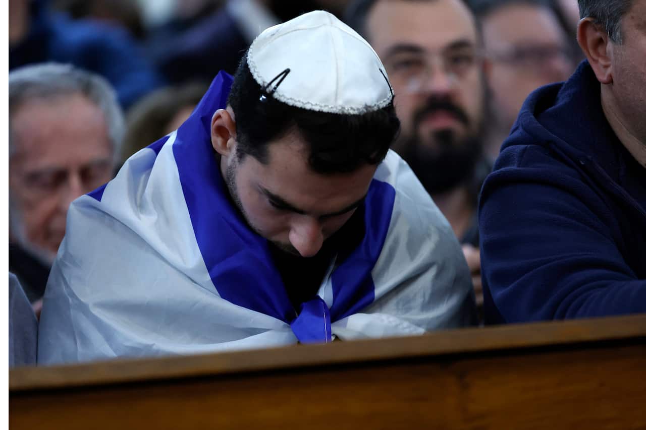 A man wrapped in an Israeli flag bows his head.
