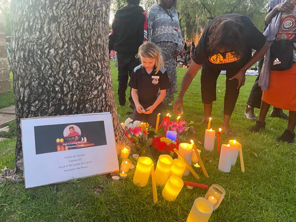 A child sits and pays respect to a vigil to Cassius Turvey in Alice Springs.