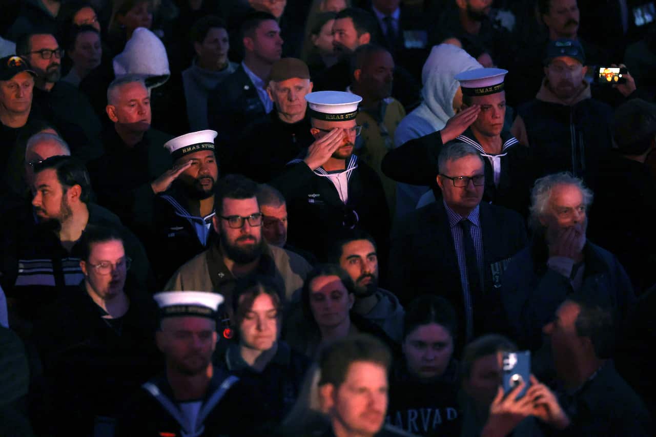 Men in uniform salute at a dawn service.