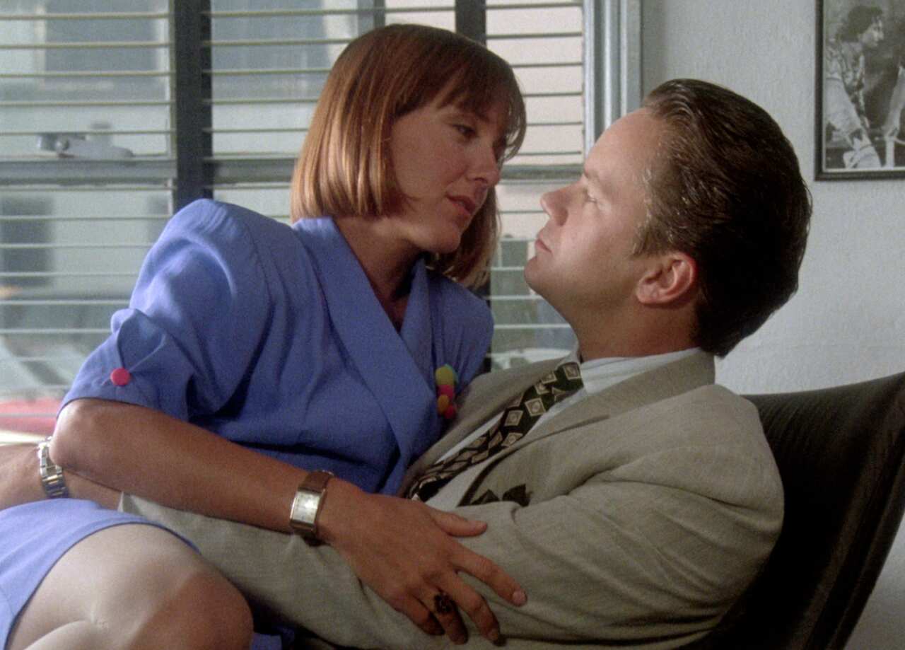 A man sits in an office chair with a lady sitting on his lap