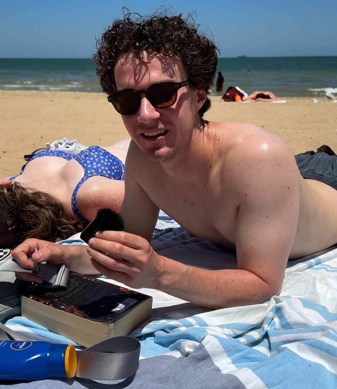 A man laying on a towel on his stomach on the beach.