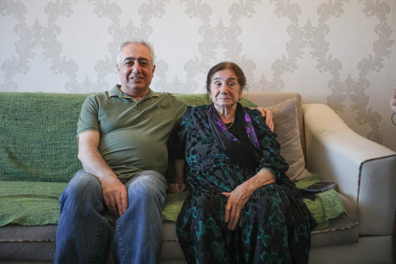 Man in green sitting on couch with his arm around older woman.