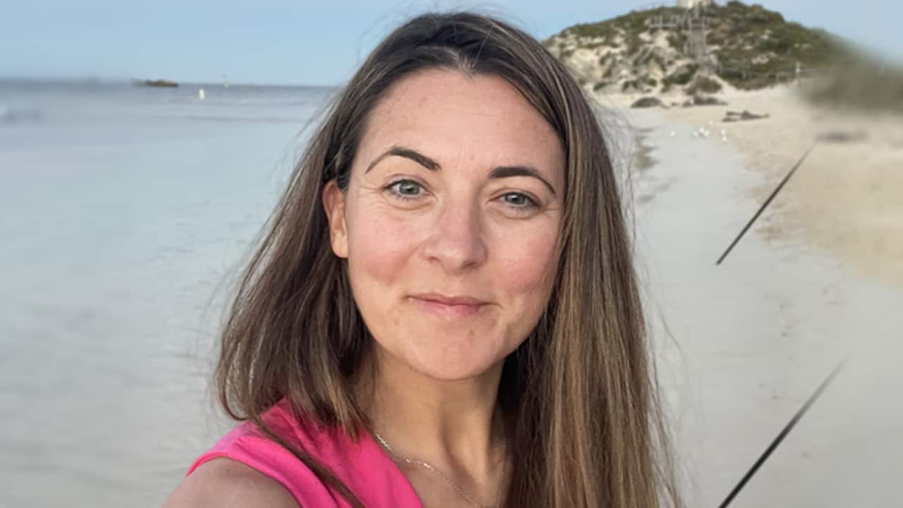 A selfie of a woman standing on the beach, smiling at the camera.
