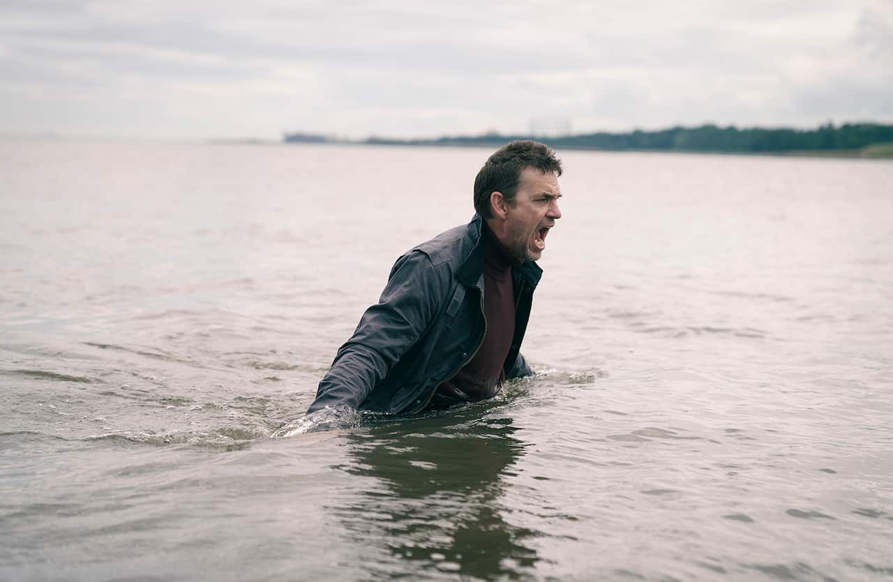 A man in a jacket stands waist deep in water, screaming.