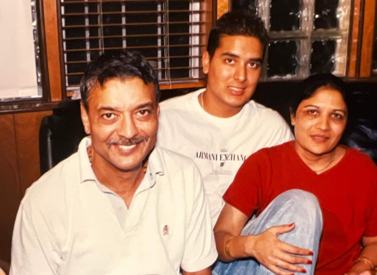 A family pose for a picture. There is a grown-up man with his dad to his left and his mum to his right.