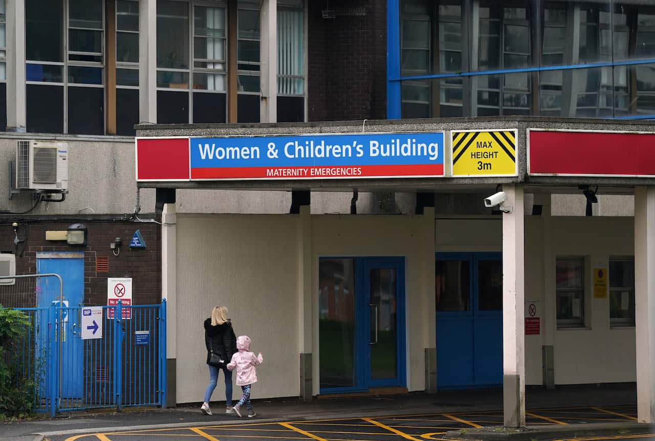 Two people walking into a hospital, with a sign reading "Women & Children's Buildig - Maternity Emergencies"