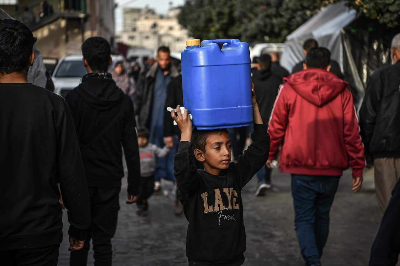 A Palestinian child carrying a blue water tank on his head