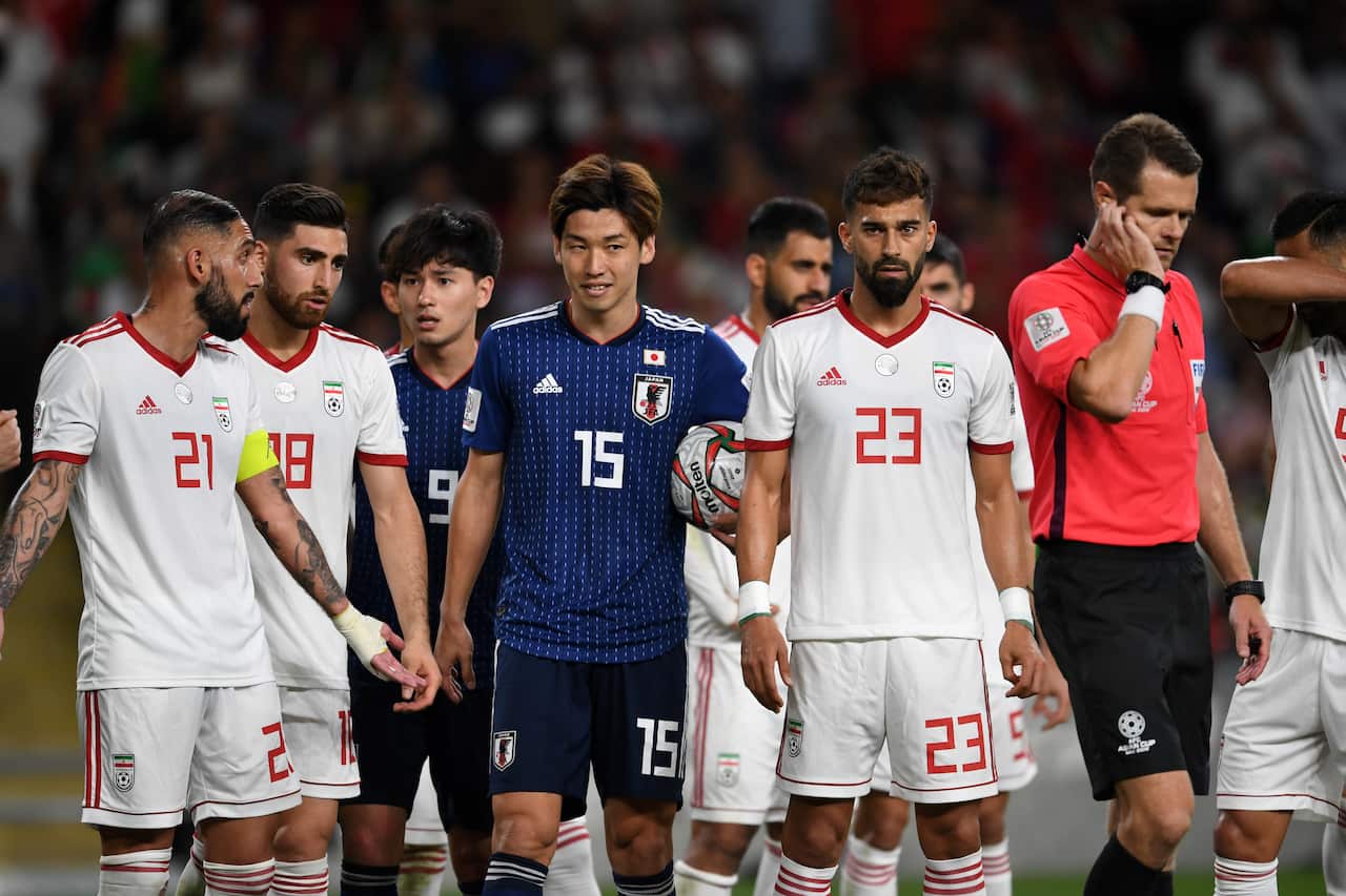 Players from two different teams lined up while a referee holds his hand to his ear