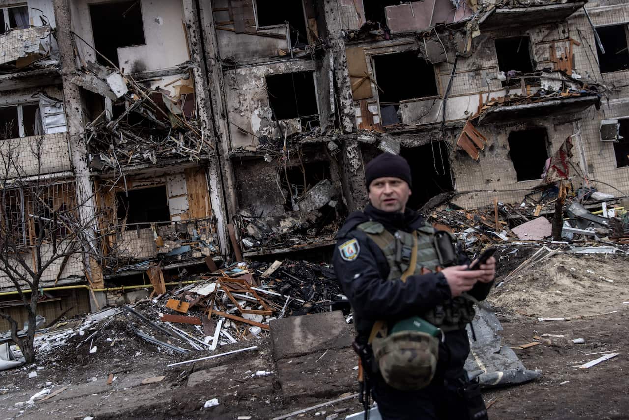 A Ukrainian police officer stands in front of a damaged residential block hit by a missile strike