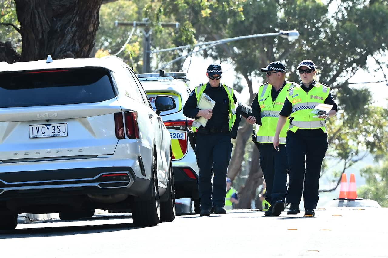 Three police officers are walking alongside two parked cars.