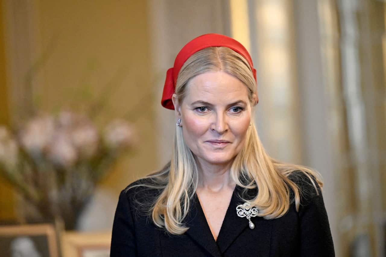 A woman with long blonde hair dressed in a black jacket and bright red hat. 