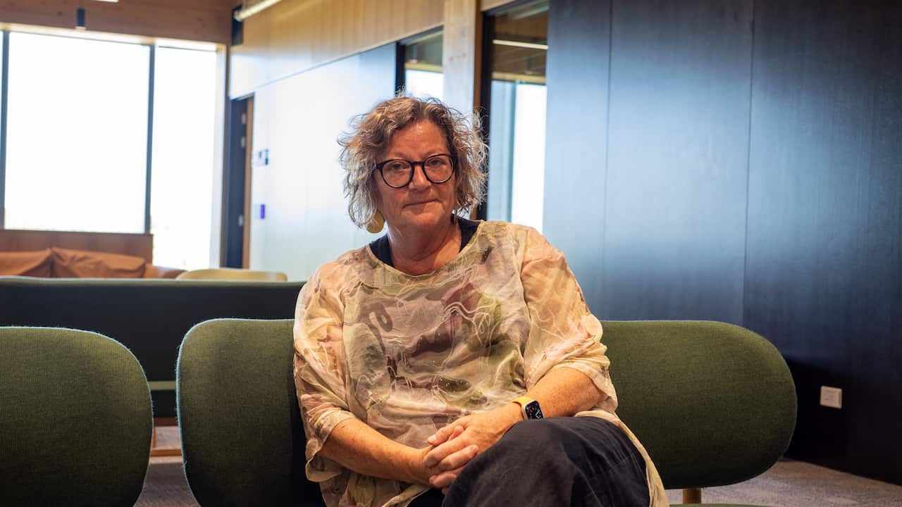 Jennifer Verduin, a middle-aged white woman with grey hair wearing a pastel patterned shirt, sits on an olive green lounge chair.