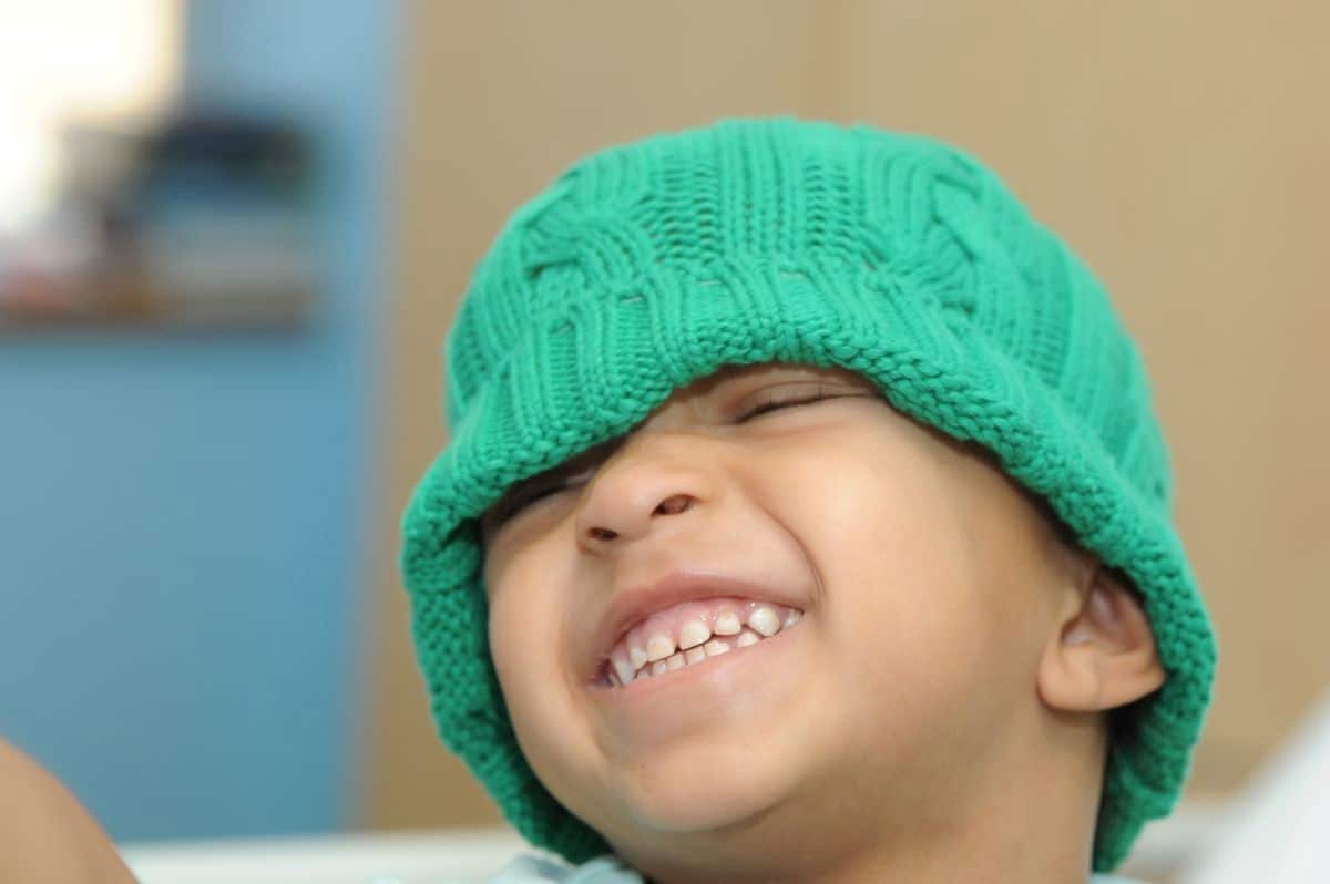 Young boy wearing a green beanie and smiling. 