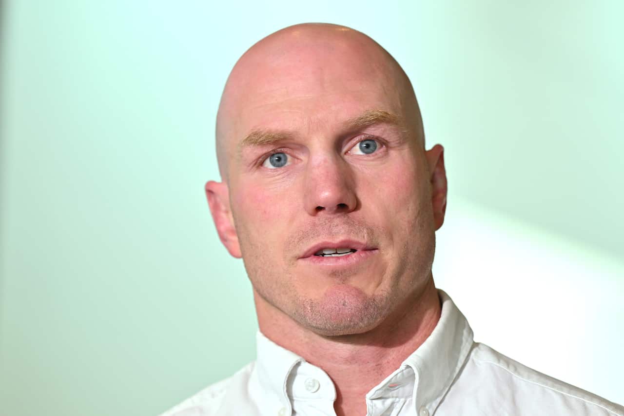 David Pocock, wearing a white shirt, standing in front of a beige wall.