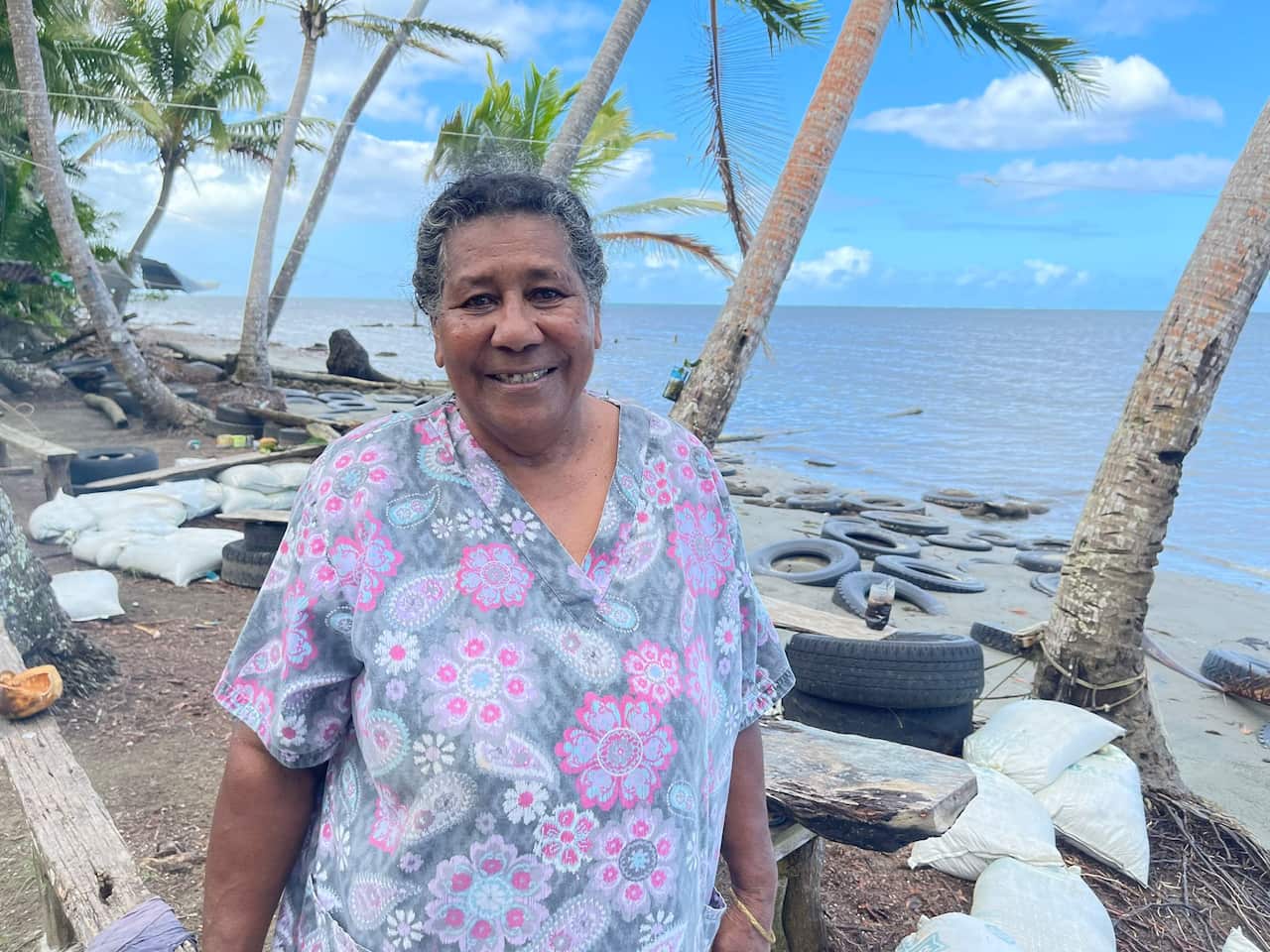 A woman standing in front of tyres and sandbags on a small section of beach with the ocean behind her.