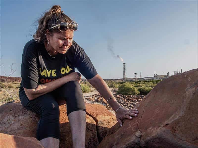 A woman in a black t-shirt is caressing a rock surface.