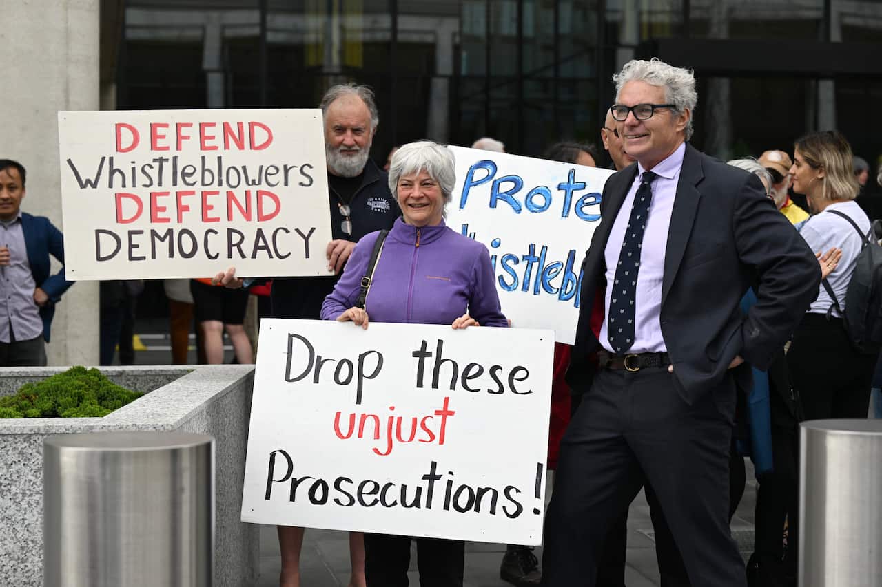 Protestors holding signs saying "defend whistblowers, defend democracy" and "drop these unjust prosecutions".