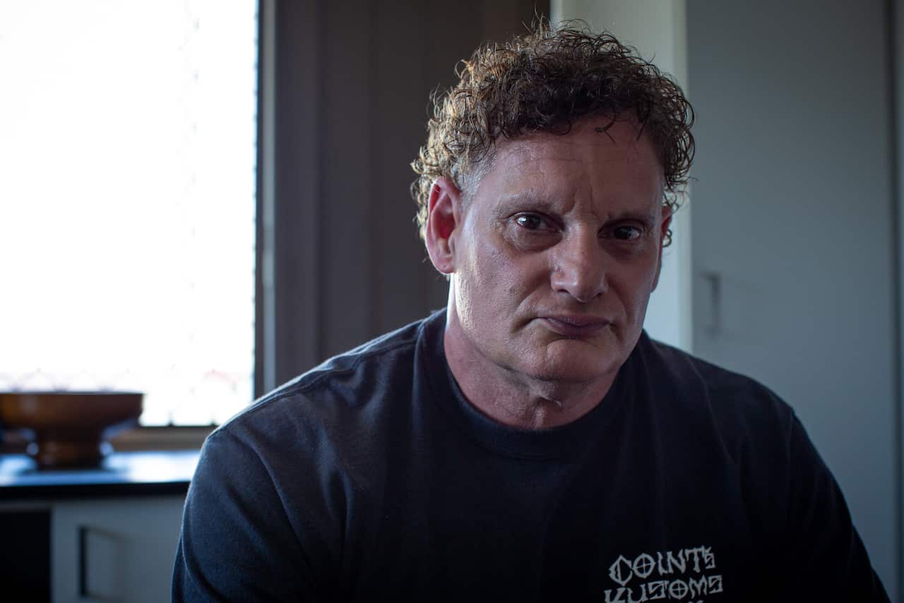 A middle-aged man with curly hair is wearing a black t-shirt and sitting at a table.