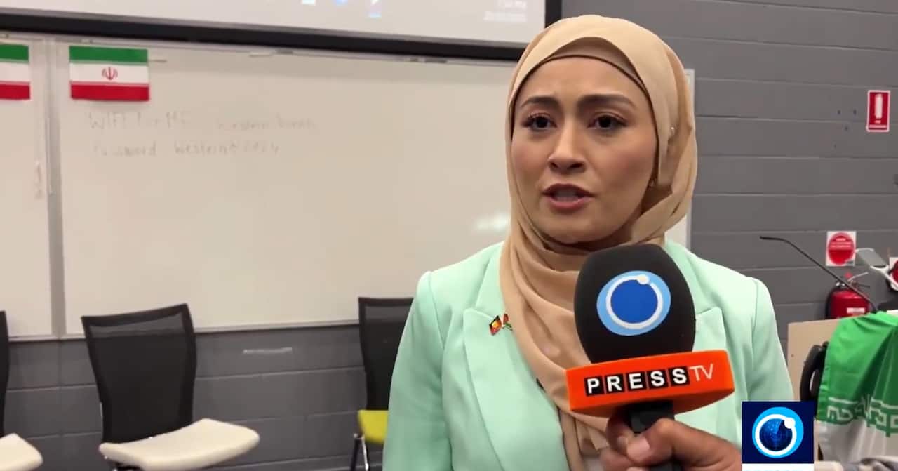 A woman wearing a mauve hijab speaks into a press microphone