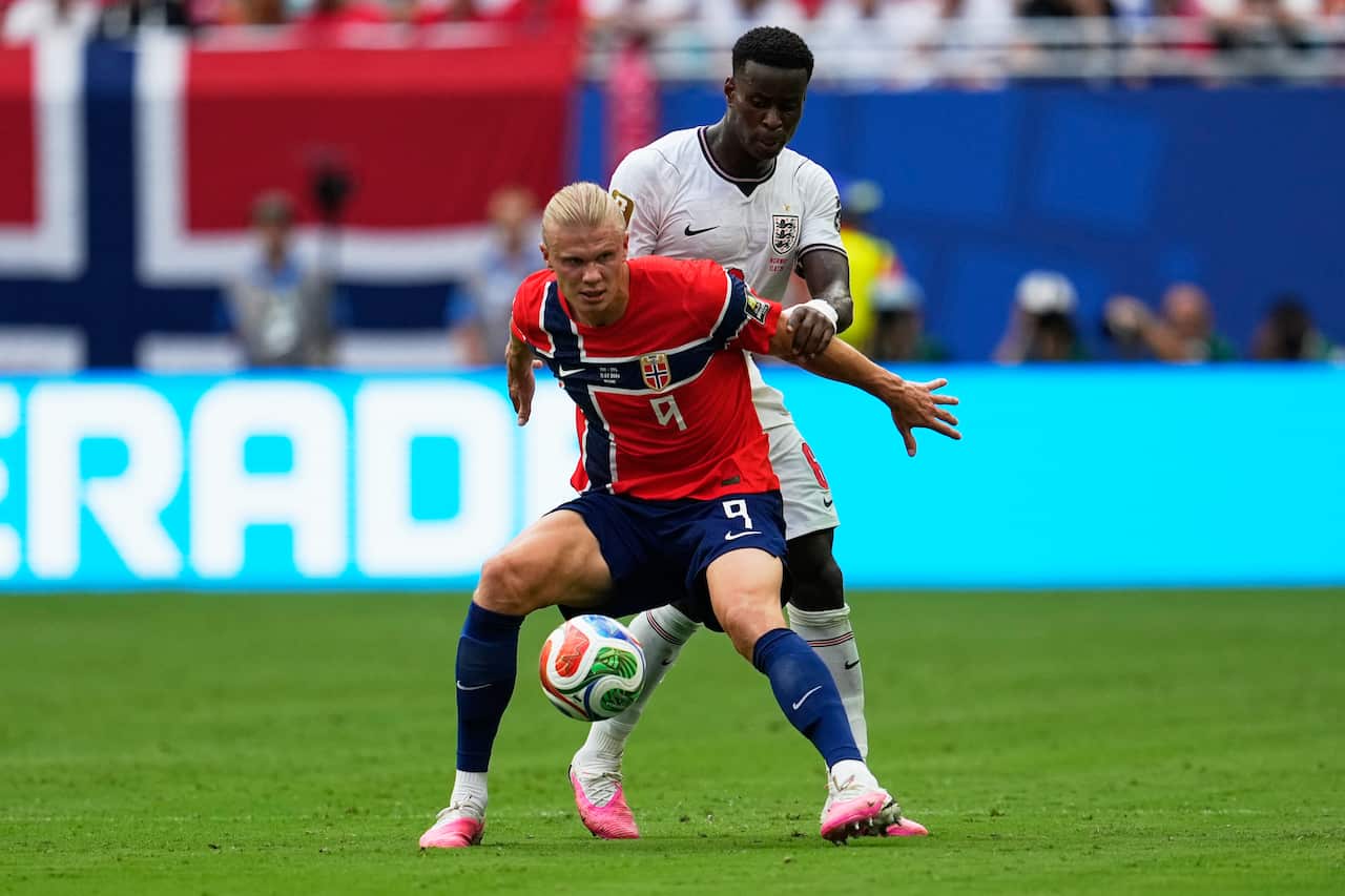 Two football players, one in red and blue and the other in white and red, tussle over a ball during a match.