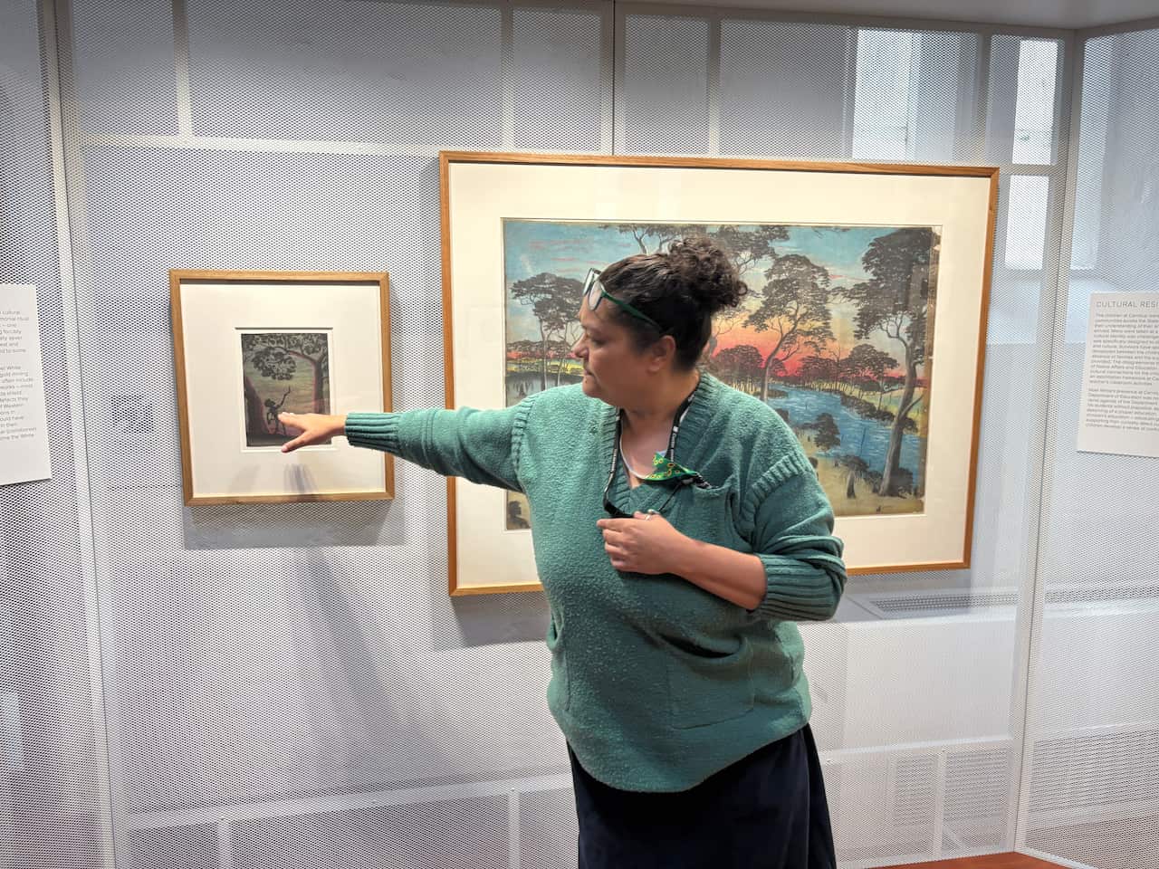 A woman pointing towards an artwork hanging on the wall beside her.