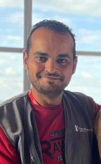 A smiling man wearing a red jumper and a vest