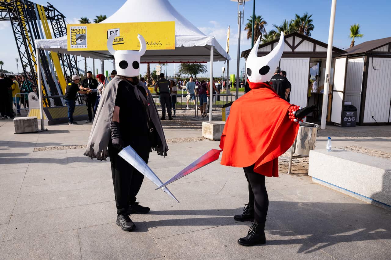 Two people dressed up as characters from the game Hollow Knight, with swords and large insect heads.