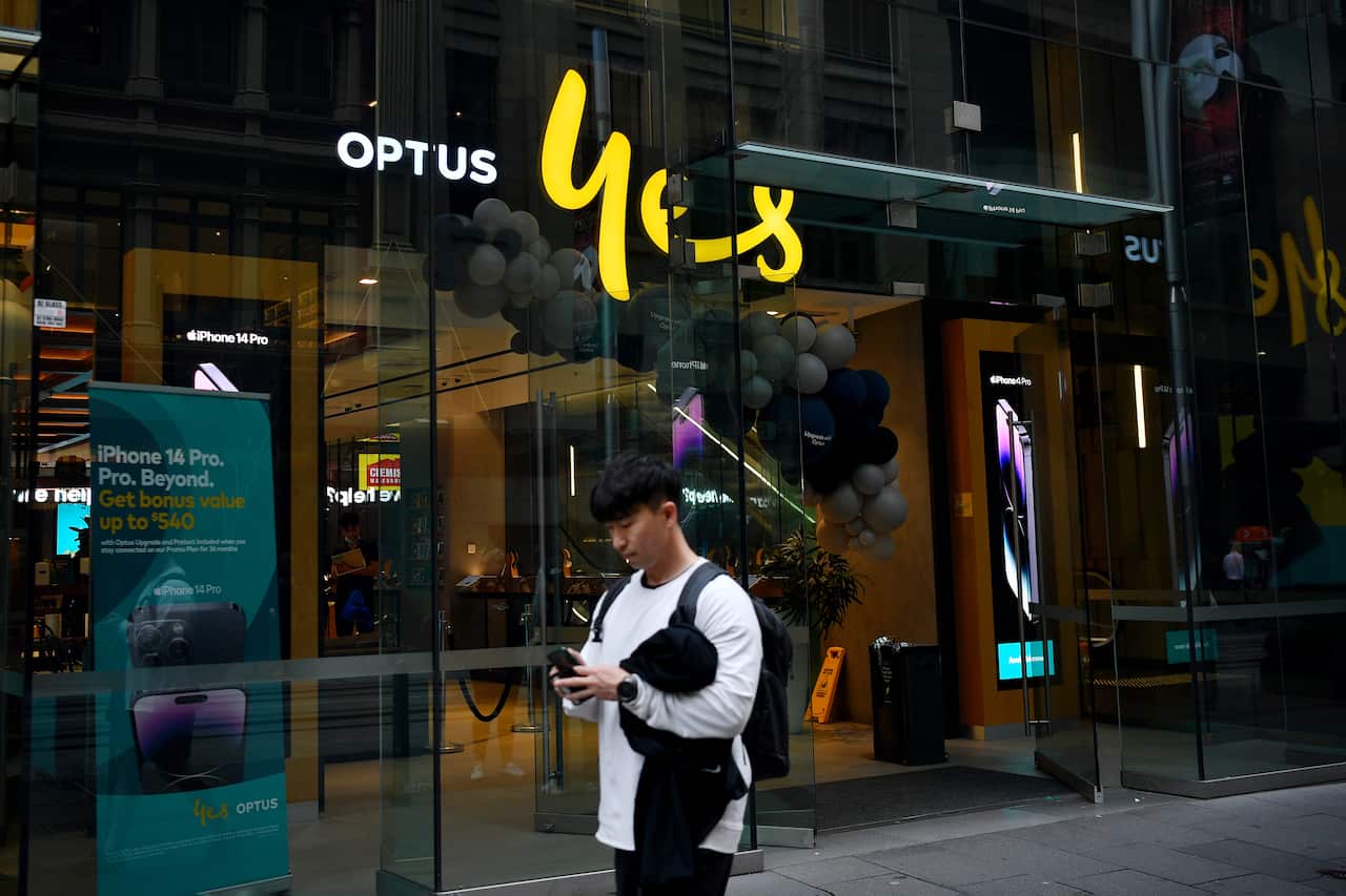 A man looks at his phone while walking past an Optus store.