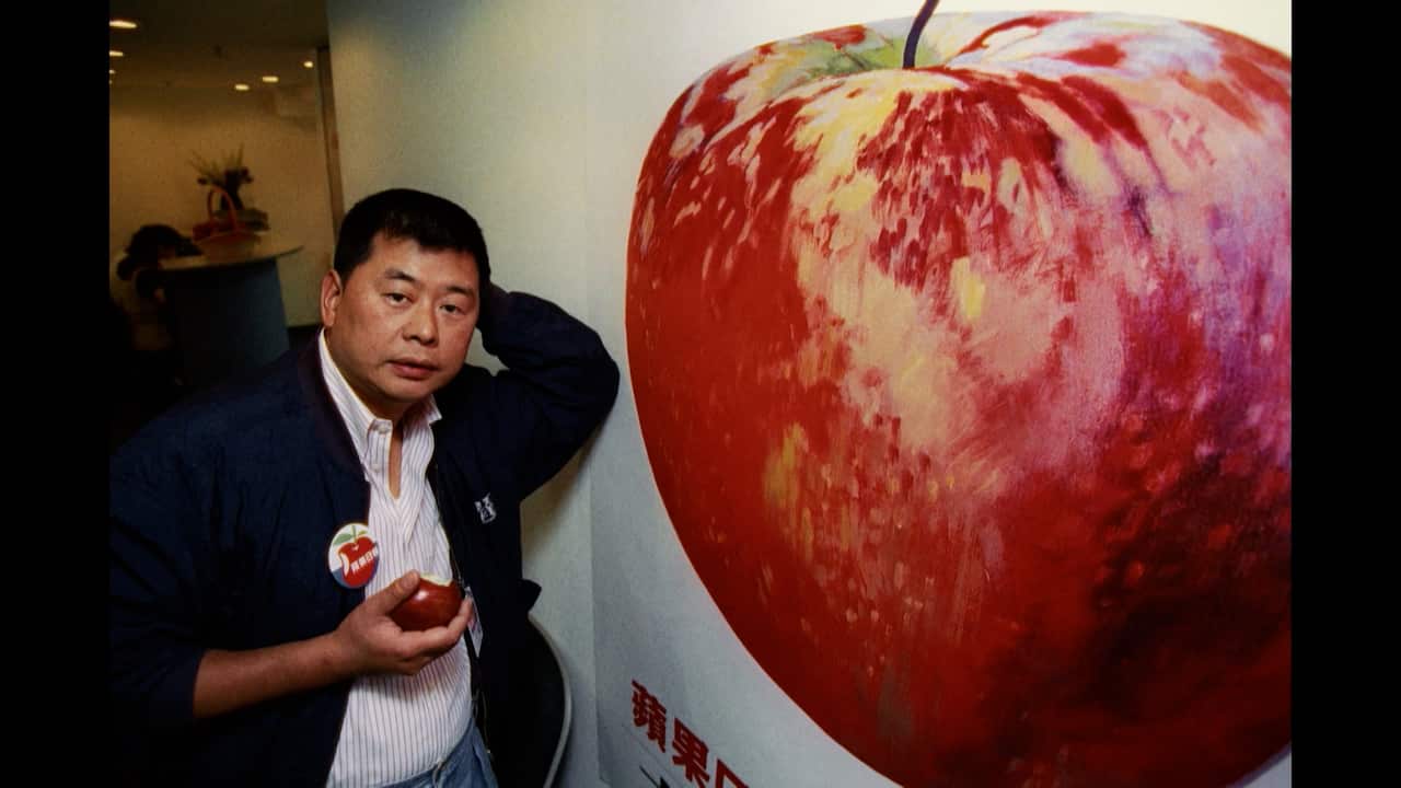 A man in a suit holding a red apple and standing next to a large 3-D mural of a red apple on a white wall