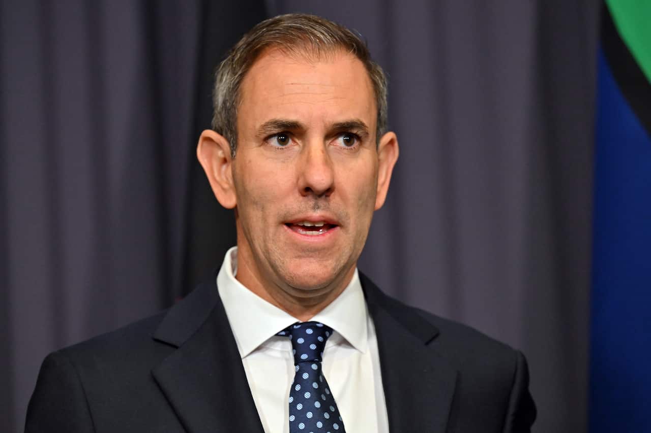 Jim Chalmers, wearing a suit and tie, standing in front of a grey curtain.