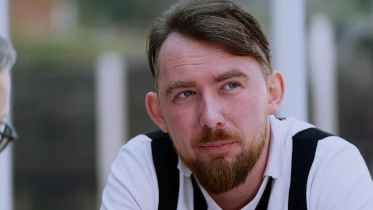 A man in his 30s with read hair and beard wearing a black-and-white jersey