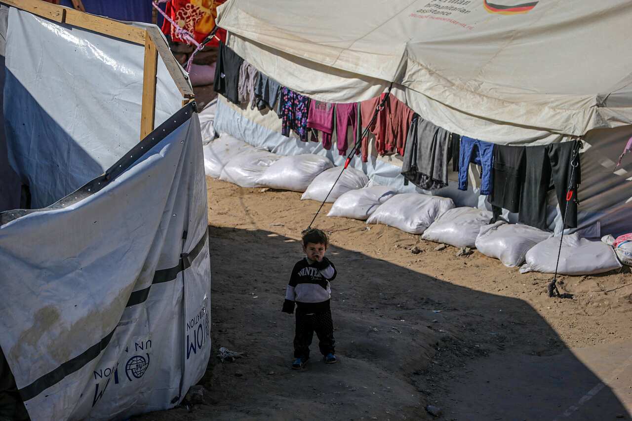 Small boy stands between tents and sand bags