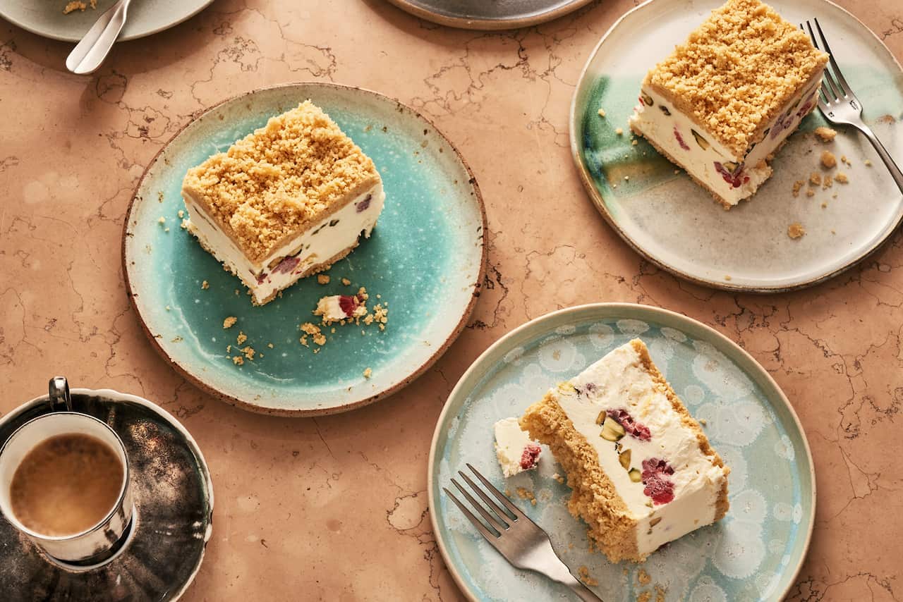 Serves of a layered ice-cream dessert sit on three different beautiful plates in tones of cream, grey and teal. A cup of tea sits nearby. 