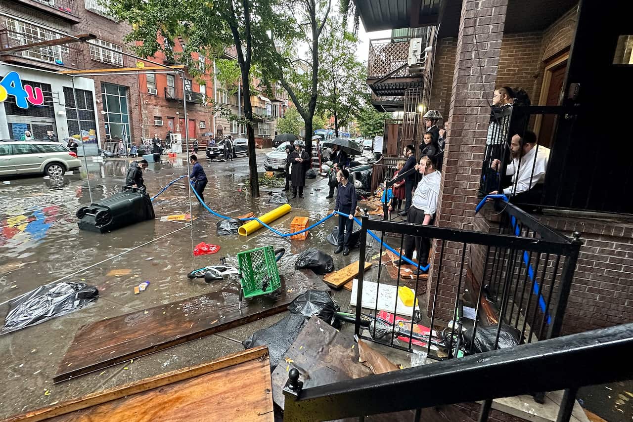 People watch as workers attempt to clear a drain in flood waters.