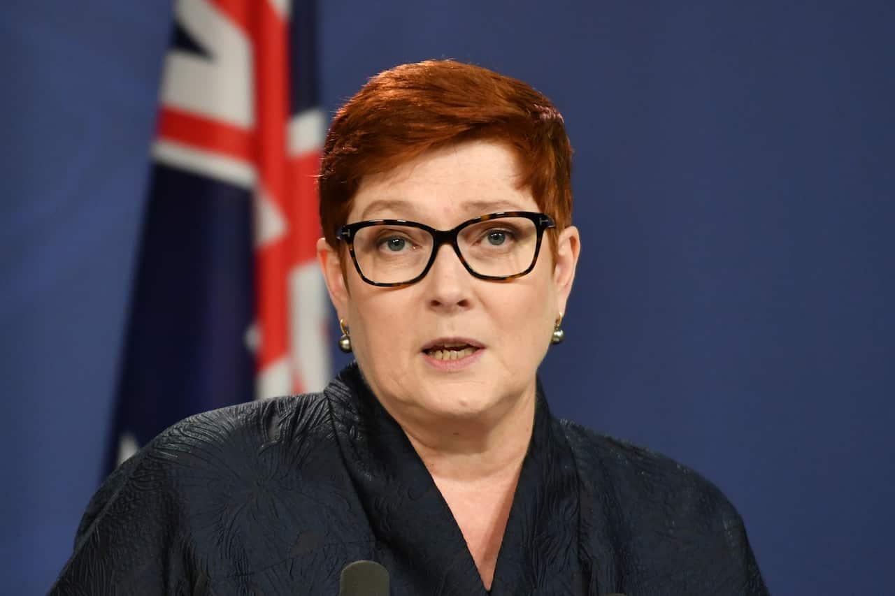 A woman speaking in front of a blue background and Australian flag