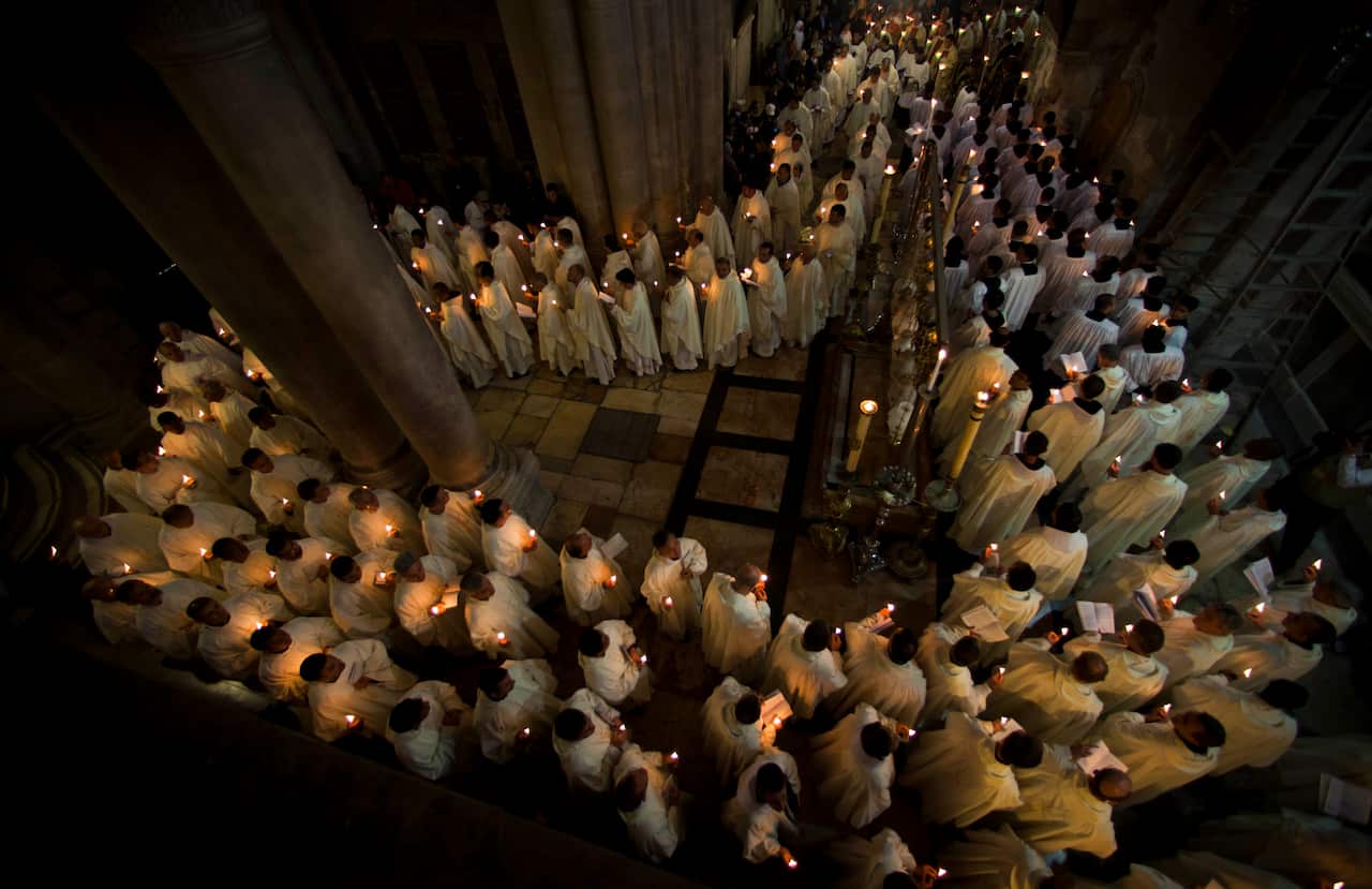 An elevated view of a large group of clergy in white vestments holding lit candles during a nighttime service at the Church of the Holy Sepulchre.