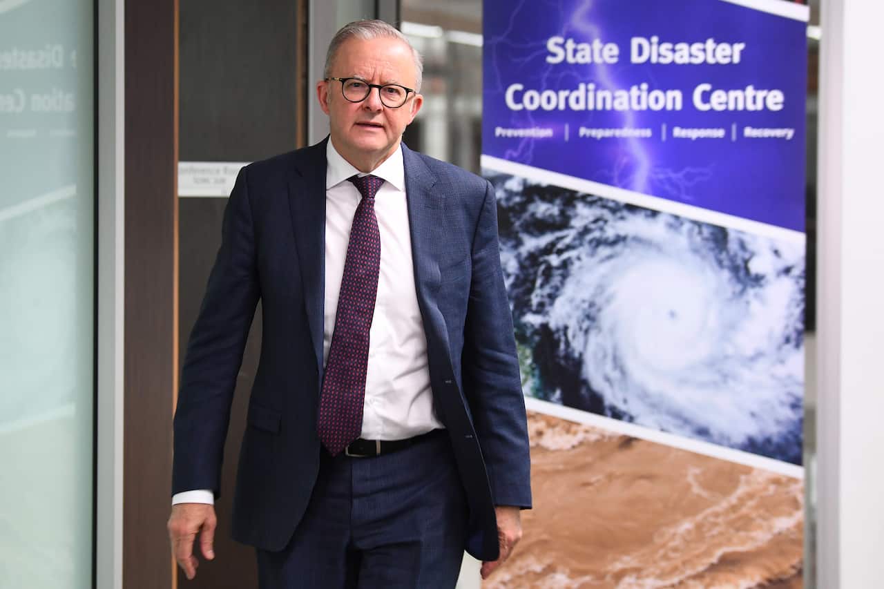 Anthony Albanese wearing a blue suit is standing in front of a poster with the words 'State Disaster Coordination Centre' written on it.