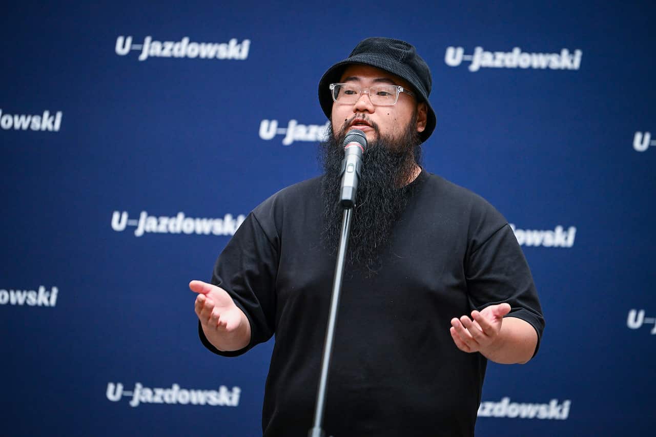 A man wearing a black tshirt and black bucket hat speaking into a microphone