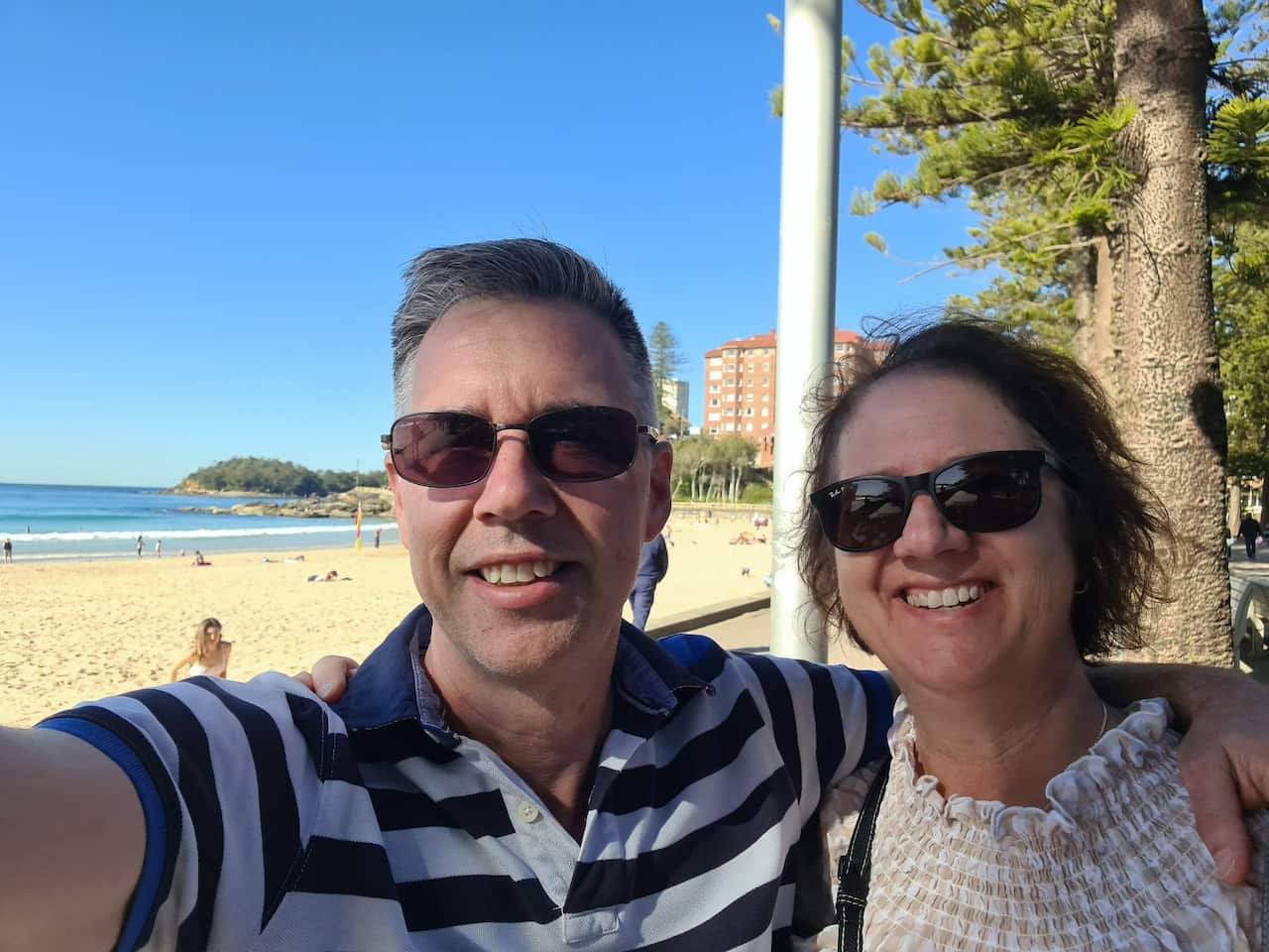 A man and a woman smile for a selfie with the beach in the background.