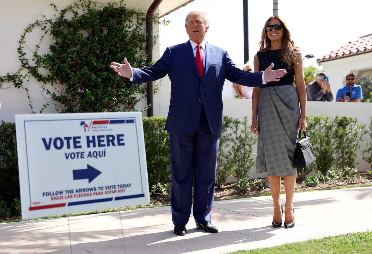 Donald and Melania Trump standing on a footpath next to a sign that reads "VOTE HERE".