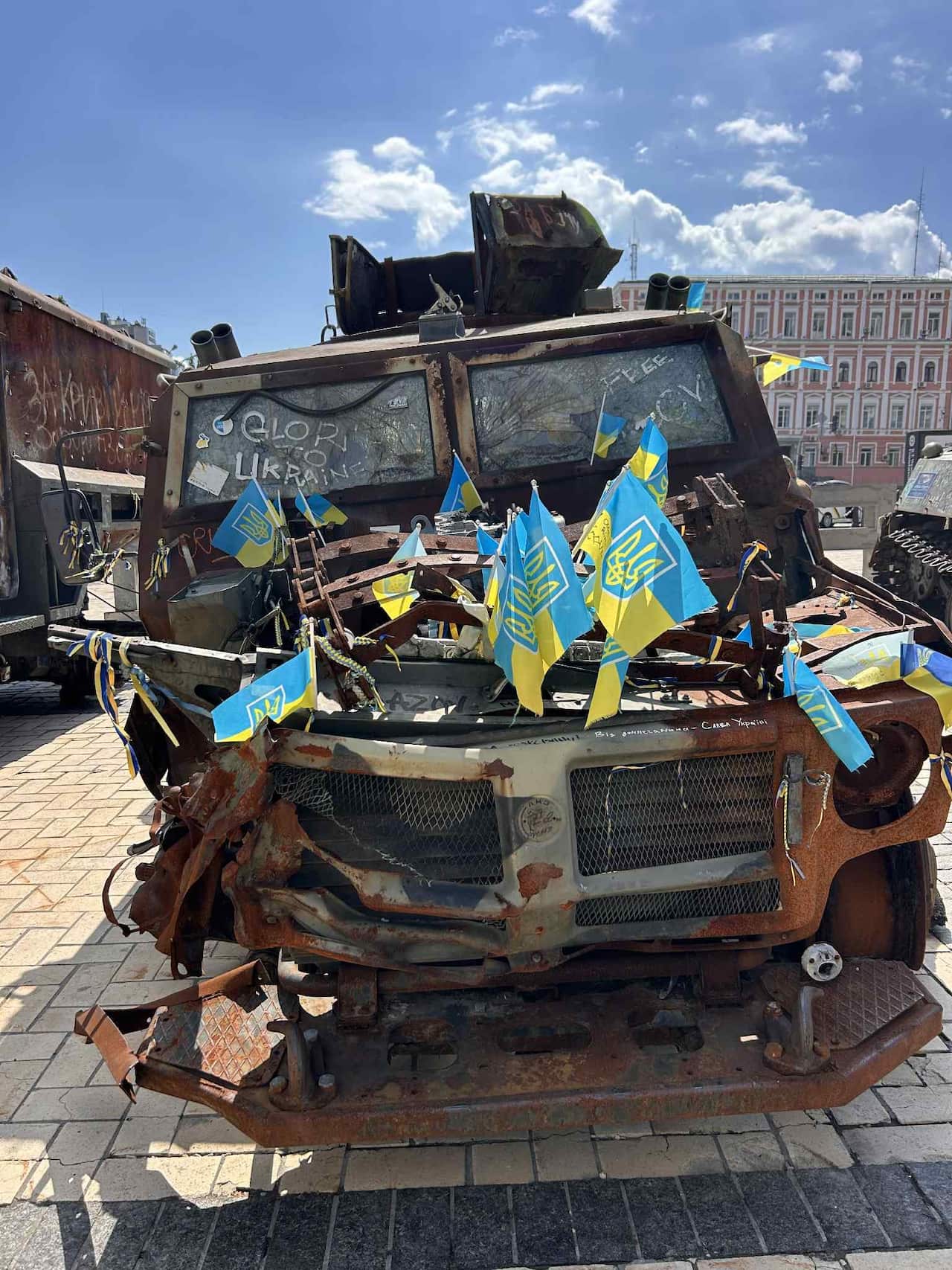 A burned-out military vehicle with blue and yellow flags stuck in it
