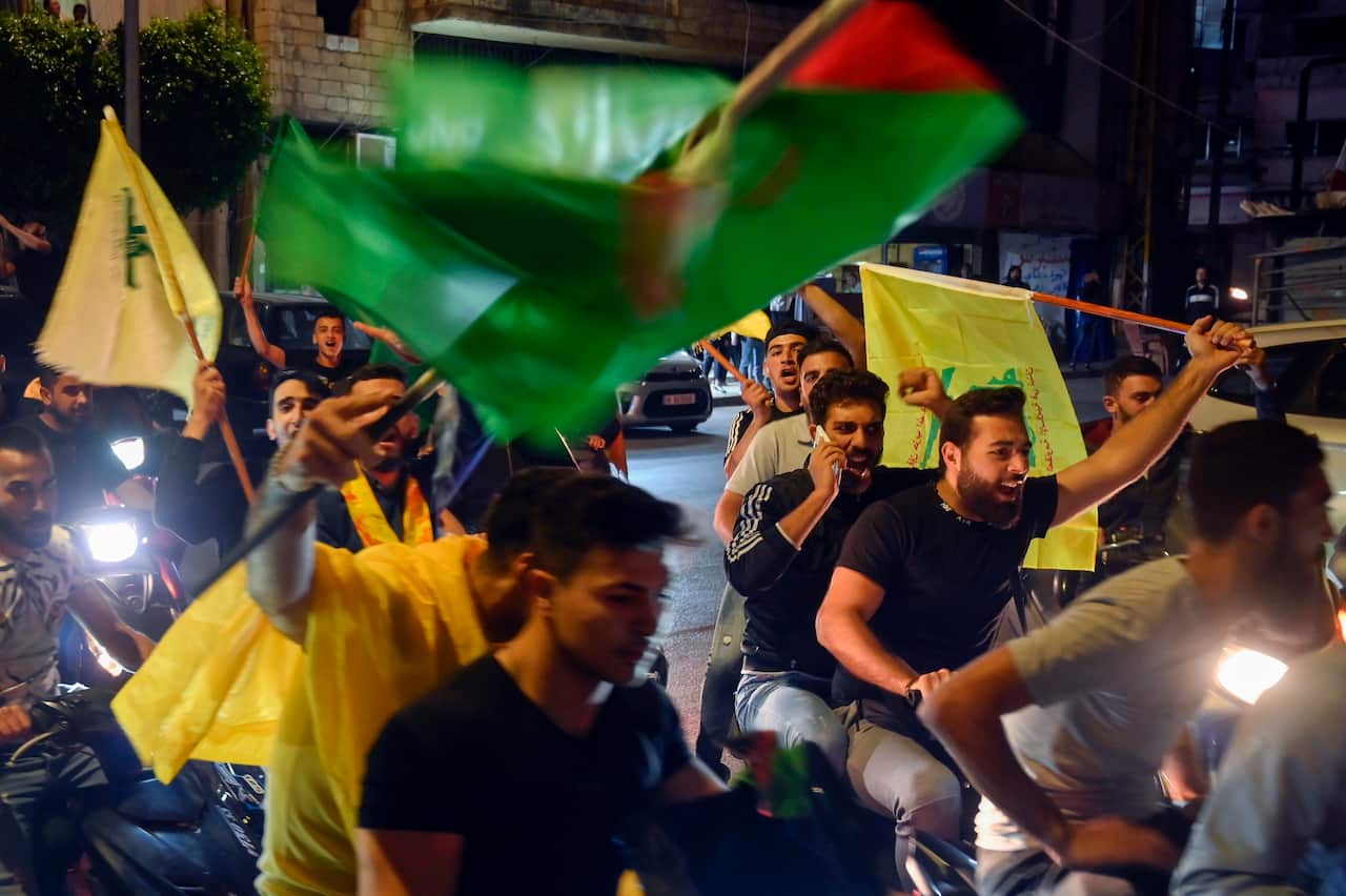 Men sit on bikes and scooters raising green and yellow flags. 