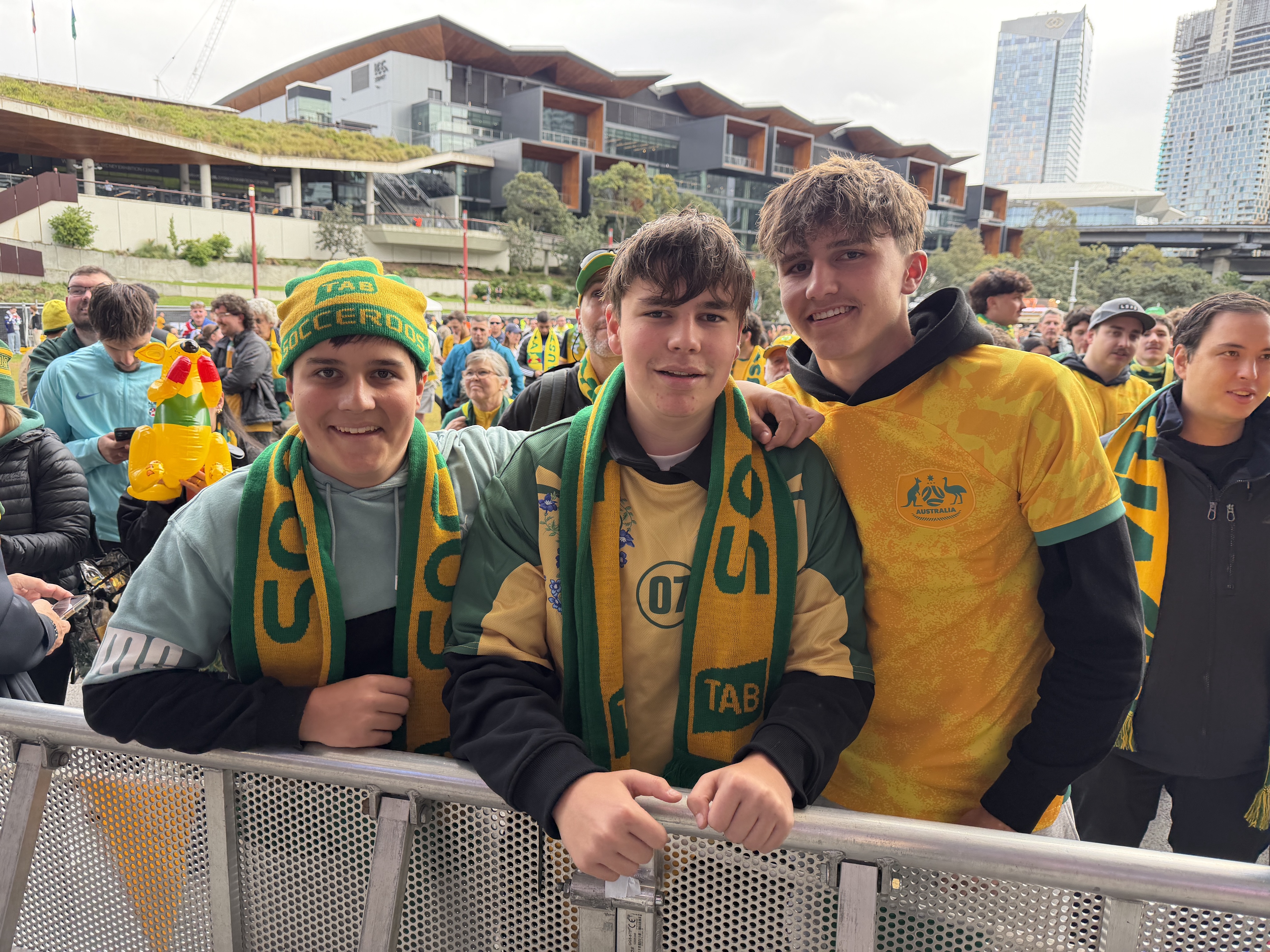 A group of three boys posing among Socceroos fans.