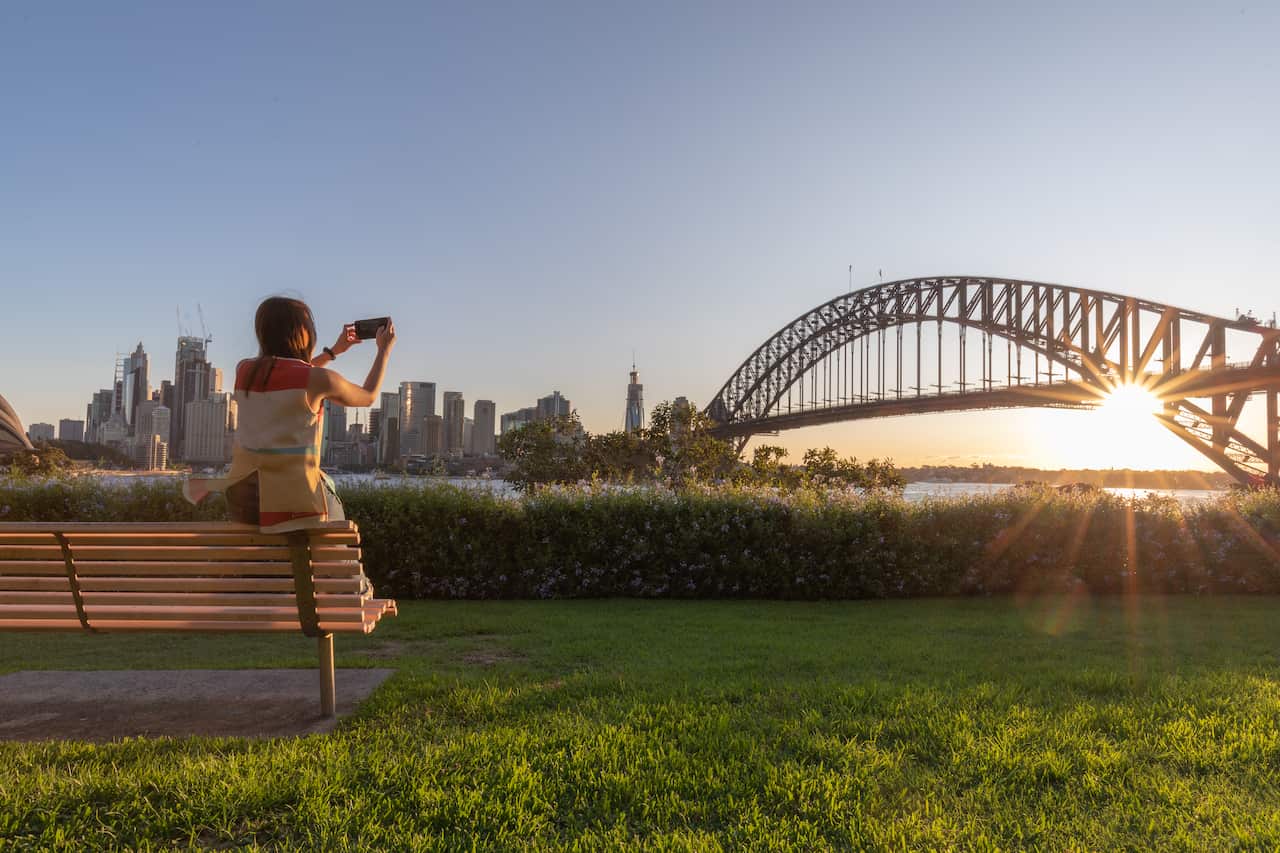 Female tourtist taking a photo Sydney Harbour Bridge with her smartphone.