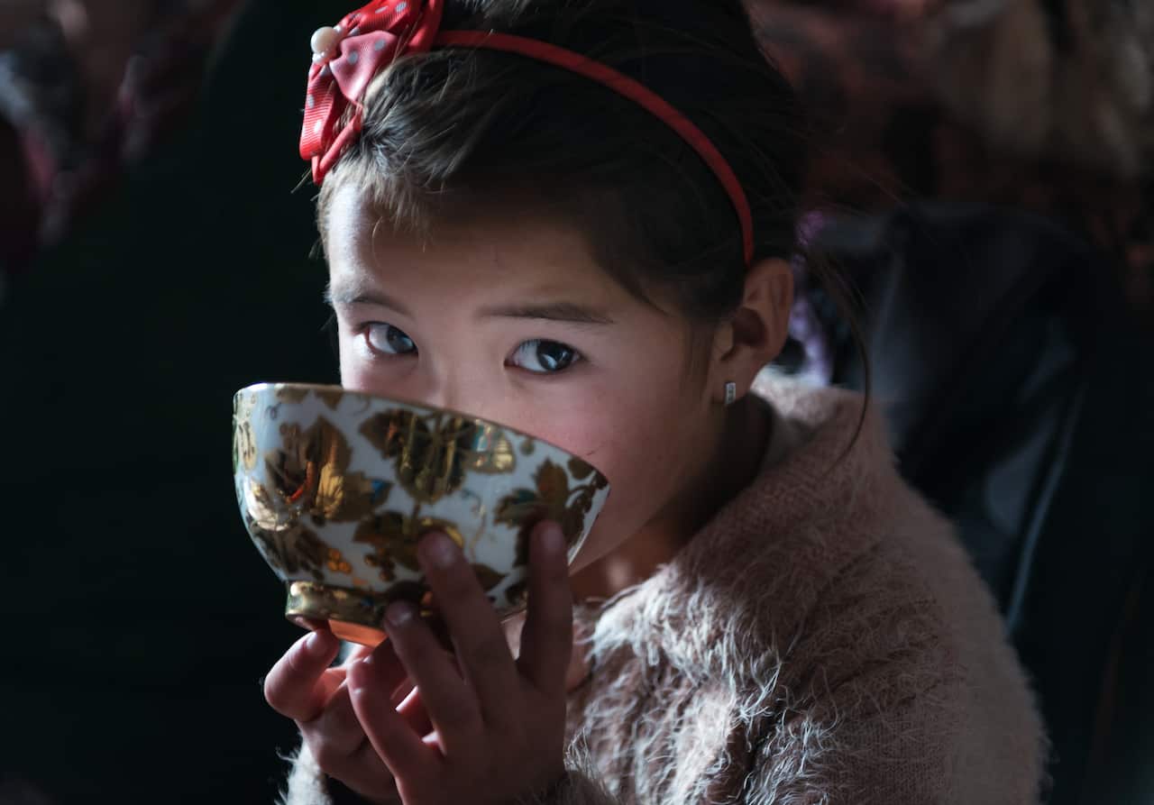 A girl with a pink bow drinks from a tea cup.
