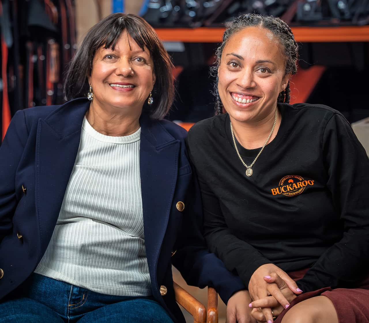 A woman in a blue blazer sits next to a woman in a black t-shirt.
