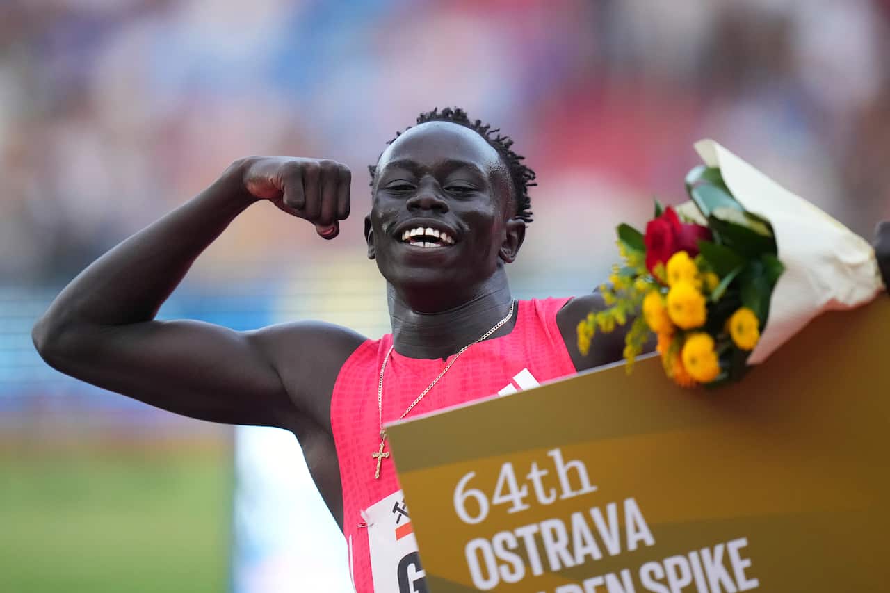 Gout Gout, wearing a red jersey, smiling and pumping his arm while holding flowers in the other.