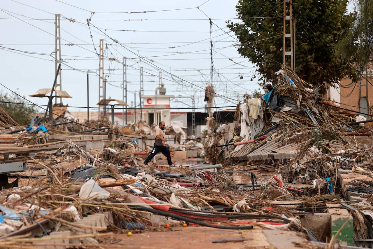 Man attempts to cross destroyed tracks left behind from floods in Spain.