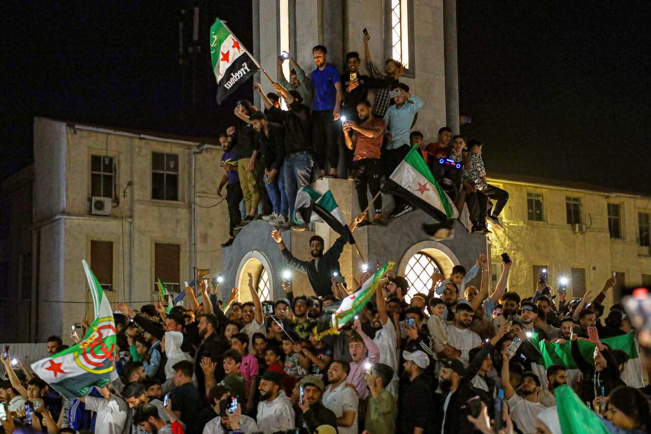 A large group of men and boys, many waving flags. Some have climbed a monument.