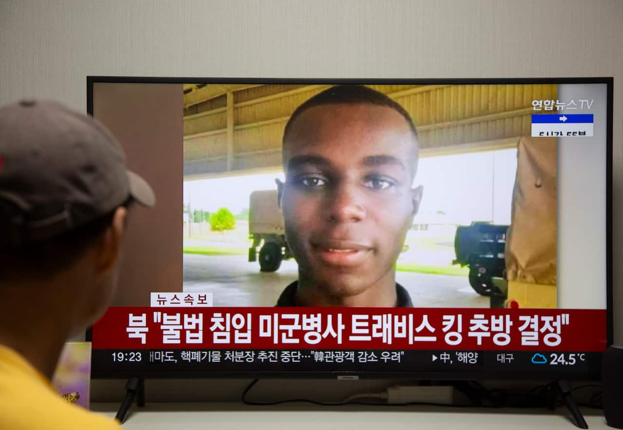 A man looks at an image of Private Travis King shown on a television. A super written in an Asian language can be seen under the image of Private King.